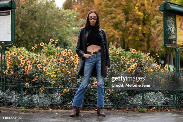 Model Moira Berntz wears skinny sunglasses, black leather jacket, black croptop, blue jeans, brown belt, and brown cowboy boots after the Chanel show...