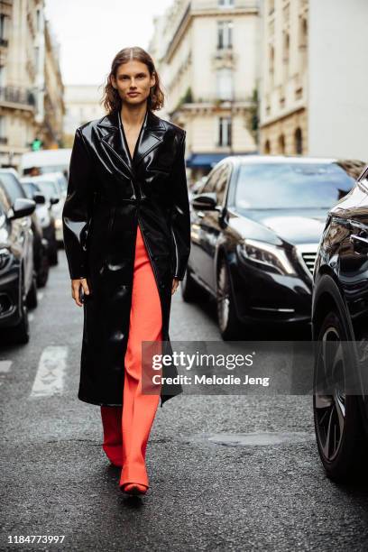 Model Giedre Dukauskaite wears a black leather Kwaiden Editions trench coat and orange pants after the Kwaiden Editions show during Paris Fashion...