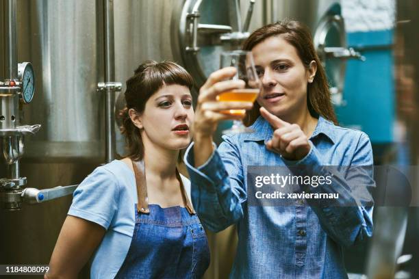 mujeres hispanas que comprueban la calidad de la cerveza artesanal en la cervecería - fábrica de cerveza artesanal fotografías e imágenes de stock