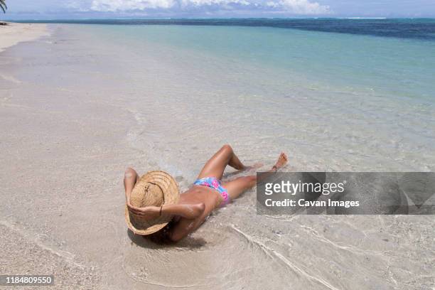 man wearing straw hat and blue speedo, tanning on idyllic sandy beach - calções de corrida imagens e fotografias de stock