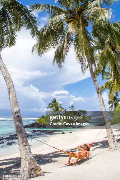 young latin man, with curly hair, wearing hat, on hammock at beach - samoa stock pictures, royalty-free photos & images