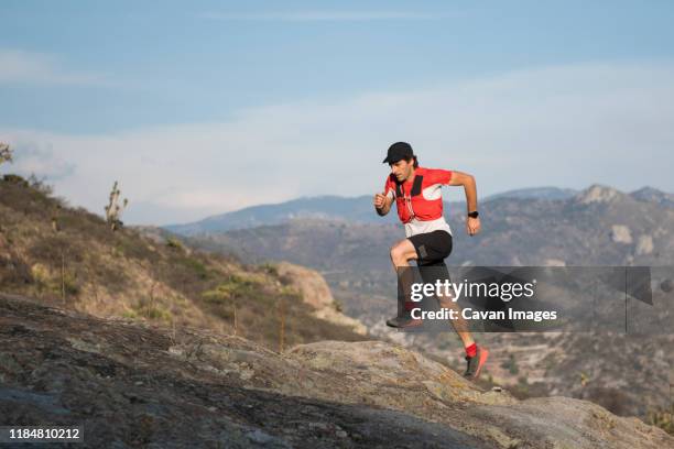 fit, athletic middle aged man running up a rocky trail during the sunset with mountains in the background in the desertic area around el arenal, hidalgo, mexico. - ultramarathon stock-fotos und bilder