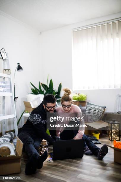 young couple moving in new home. sitting on floor and relaxing after cleaning and unpacking. looking something on laptop. - couple seated apartment hipster imagens e fotografias de stock