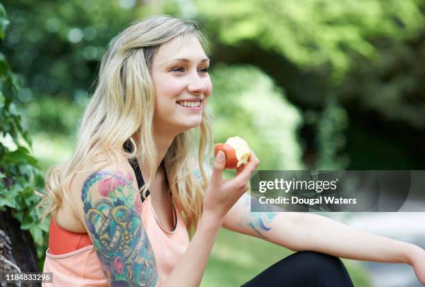 tattooed woman sitting in countryside eating apple. - eat apple stock pictures, royalty-free photos & images