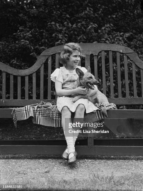 The Royal Princess Elizabeth with a Pembroke Welsh Corgi dog sitting on a bench at her home at 145 Piccadilly, London, UK, July 1936.