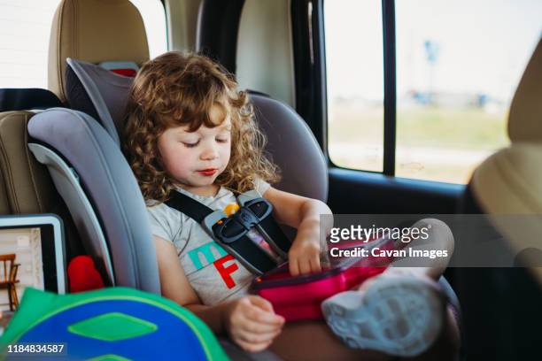 young girl sitting in a car seat and eating lunch on a road trip - jause stock-fotos und bilder