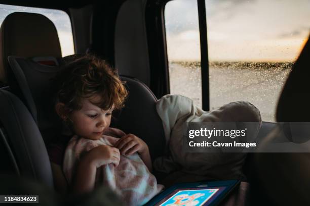 young girl playing educational game on car ride home while it rains - girl in car with ipad stock-fotos und bilder