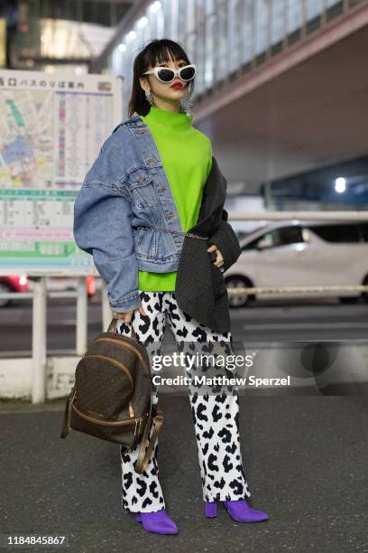 Guest is seen wearing neon green sweater, denim/blazer constructed jacket, cow print pants, purple heels, Louis Vuitton backpack during the Rakuten...