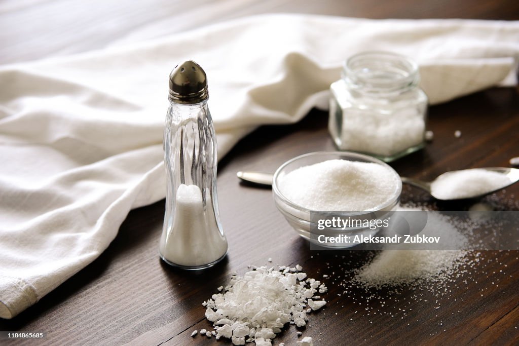 Natural, organic, sea, white salt in a spoon, in a Cup, in a salt shaker, poured on a wooden table. Next to the linen towel. The concept of cooking healthy food, cosmetology. Selective focus
