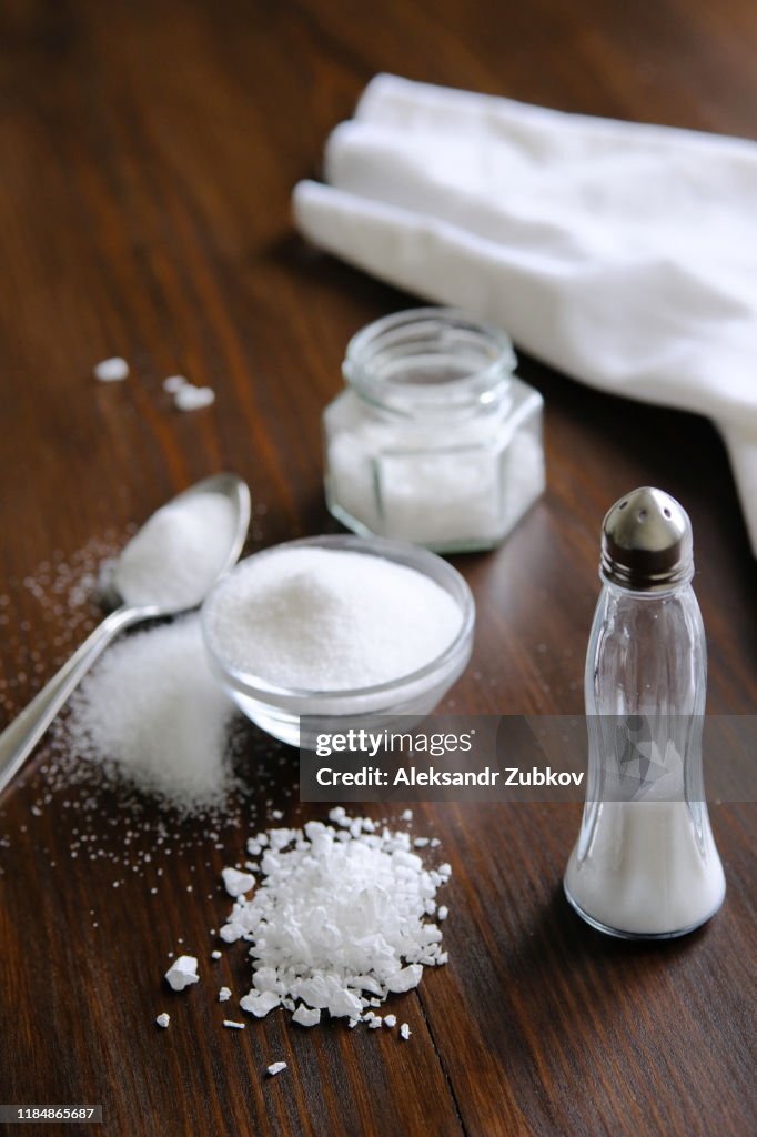 Natural, organic, sea, white salt in a spoon, in a Cup, in a salt shaker, poured on a wooden table. Next to the linen towel. The concept of cooking healthy food, cosmetology. Selective focus