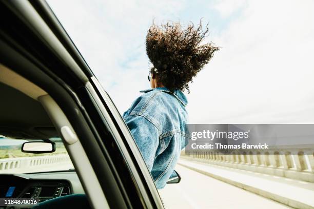 rear view of woman leaning out of car window with hair blowing in wind - autonom stock-fotos und bilder