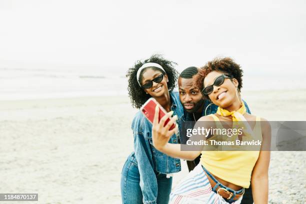 smiling friends taking selfie with smart phone on beach - blue sky friends stock pictures, royalty-free photos & images