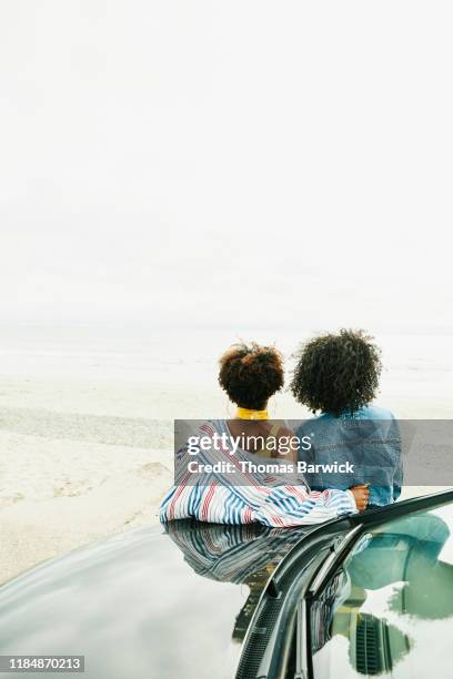 female friends leaning against hood of car and enjoying view of ocean - reflexo cabelo pintado imagens e fotografias de stock