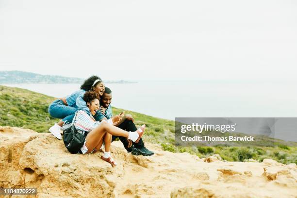 laughing and embracing friends taking selfie with smart phone while sitting at ocean lookout in park - group of beautiful people stock pictures, royalty-free photos & images