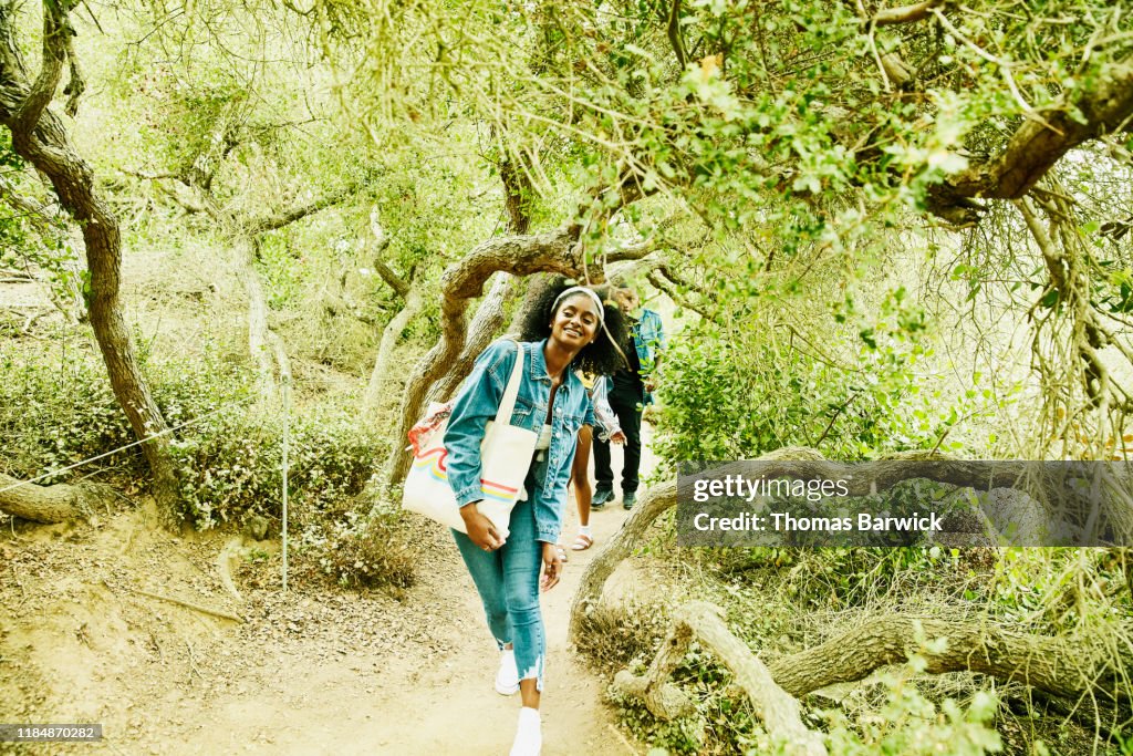 Smiling woman leading friends through tunnel of trees while exploring park