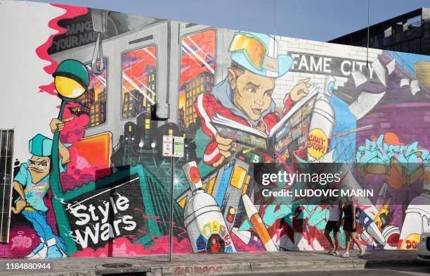 People walk in front a mural in Wynwood district street art in Miami on November 26, 2019. / RESTRICTED TO EDITORIAL USE - MANDATORY MENTION OF THE...