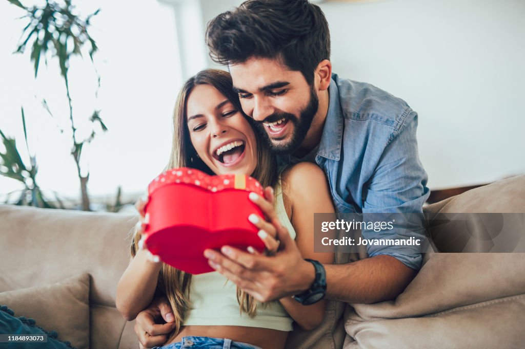 Feliz pareja con caja de regalo abrazando en casa.