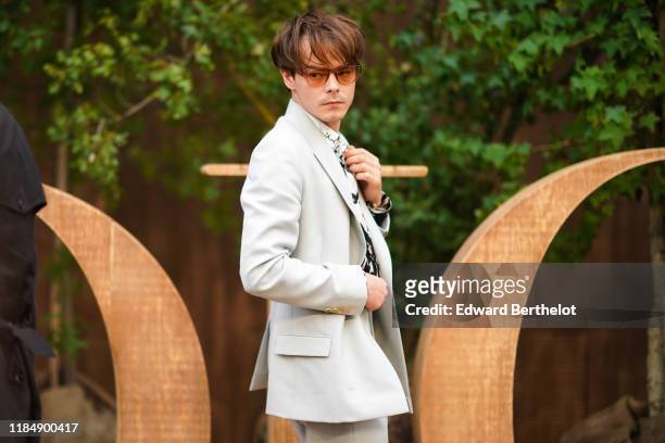 Charlie Heaton wears sunglasses, a white shirt with a black design print, a light grey suit, outside Dior during Paris Fashion Week - Womenswear...