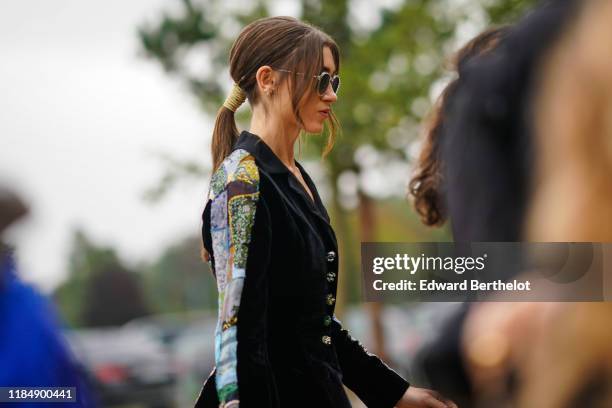 Natalia Dyer wears sunglasses, a black velvet jacket with glittering colorful inserts on the sleeves, outside Dior during Paris Fashion Week -...