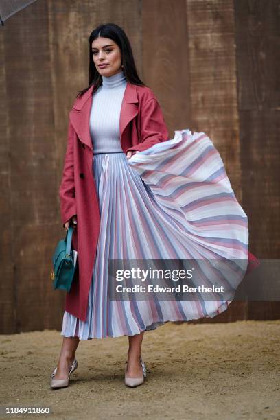 Aida Domenech wears a red trench coat, a pale blue turtleneck pullover, a pleated skirt, a green bag, outside Dior during Paris Fashion Week -...