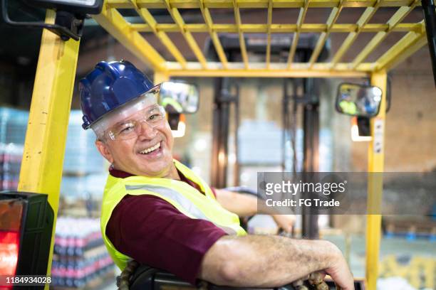 porträt eines lächelnden ingenieurs, der einen gabelstapler im lager fährt - meldebote stock-fotos und bilder