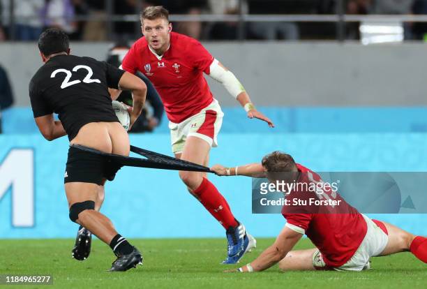 New Zealand player Anton Lienert-Brown has his shorts pulled at in the tackle by Wales player Hallam Amos as Dan Biggar looks on during the Rugby...