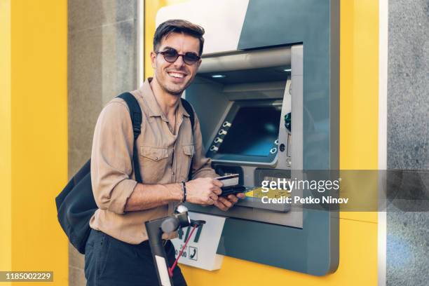 young man at the atm on the street - man atm smile stock pictures, royalty-free photos & images