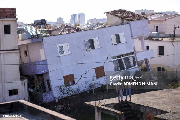 People stand in front of a collapsed building in the town of Durres, western Albania on November 27 after an earthquake hit Albania. - Albania was in...