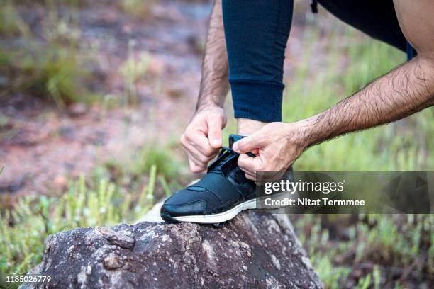 active lifestyle and nature concept. close-up of male athlete tying shoelace on cliff rock at mountain peak. - shoelaces ストックフォトと画像