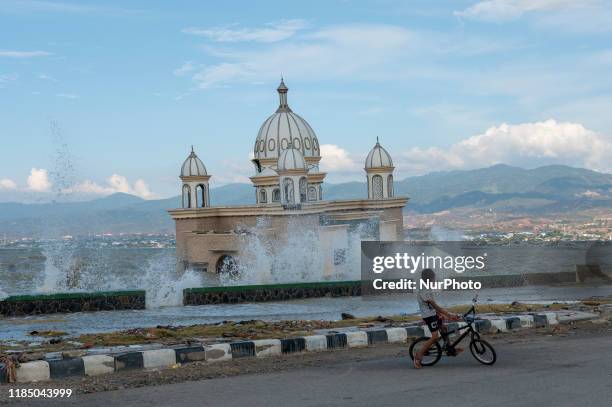 Child plays a bicycle against the backdrop of a high tidal wave near the mosque that collapsed into the sea on Kampung Lere Beach, Palu Bay, Central...