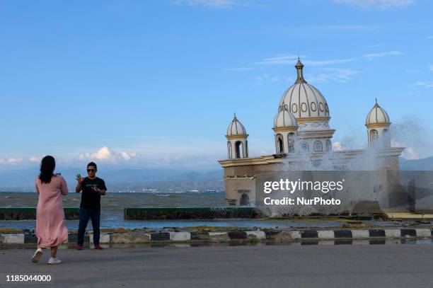 Residents take pictures against the backdrop of high tide water waves near the mosque that collapsed into the sea at Pantai Kampung Lere, Palu Bay,...