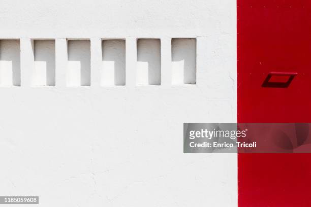 photograph of a white wall with excavated rectangles; red painted steel door. minimal background. - blue house red door stock pictures, royalty-free photos & images