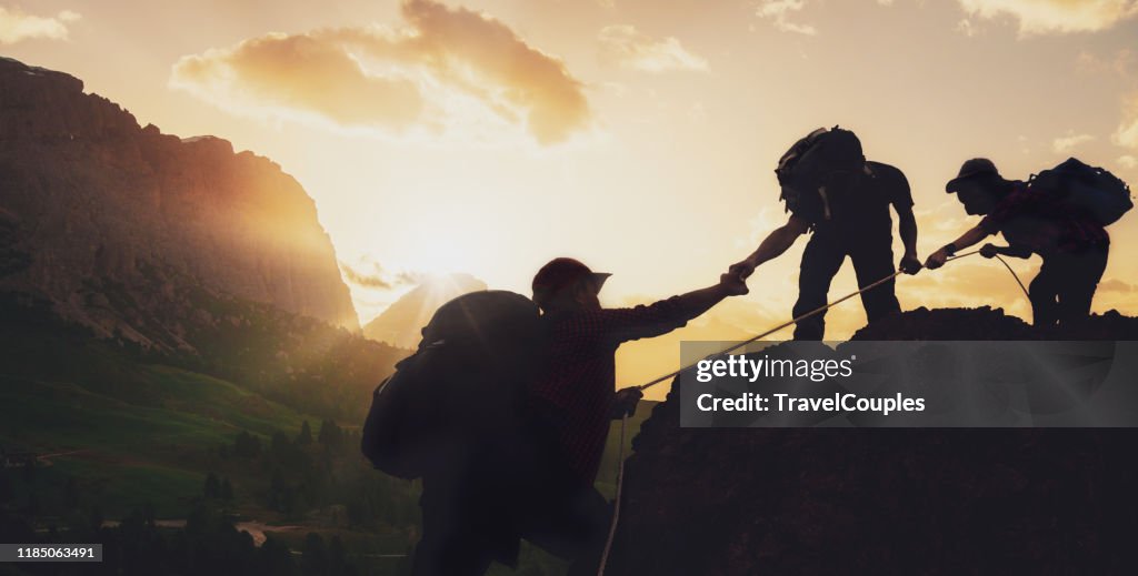 Young asian three hikers climbing up on the peak of mountain near mountain. People helping each other hike up a mountain at sunrise. Giving a helping hand. Climbing. Helps and team work concept