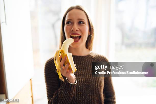 junge fit frau peeling und essen eine reife banane in der küche - banane essen stock-fotos und bilder