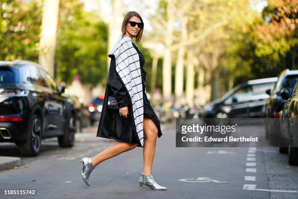 Landiana Cerciu wears sunglasses, a black long coat with white checked inner lining, a bag, silver pointy shoes, outside Shiatzy Chen, during Paris...