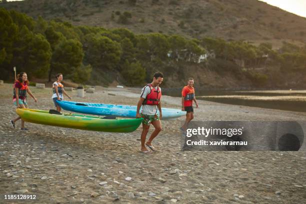 middle-aged spanish friends carrying kayaks to water at dawn - carrying kayak stock pictures, royalty-free photos & images