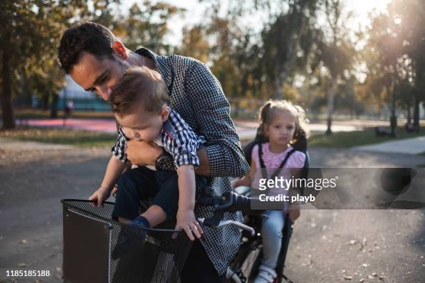 vater fährt mit seinen kindern auf einem kindersitz fahrrad - fahrradsattel stock-fotos und bilder