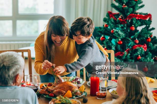 feliz madre y su hijo divirtiéndose mientras sostiene la pierna de pavo asado - christmas turkey fotografías e imágenes de stock