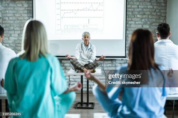 mature female doctor leading yoga class in a board room. - nurse meditating stock pictures, royalty-free photos & images