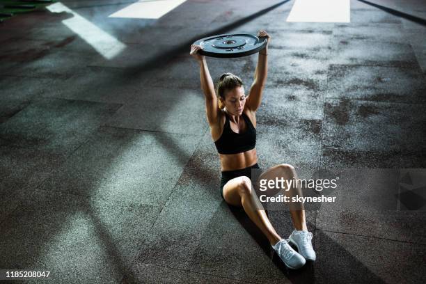 gespierd bouwen vrouwelijke atleet doen abdominale oefeningen met barbell schijf in een sportschool. - sit ups stockfoto's en -beelden