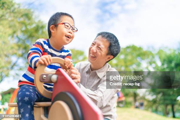 niño con síndrome de down disfrutando con su padre en el parque público - discapacidades físicas o mentales fotografías e imágenes de stock
