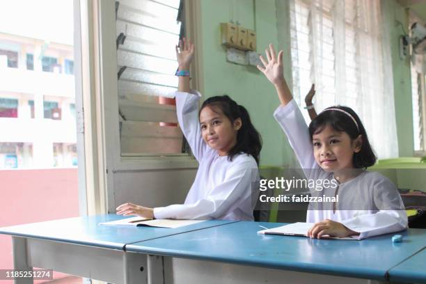 two schoolgirls raising their hands in a classroom - malaysia school stock pictures, royalty-free photos & images
