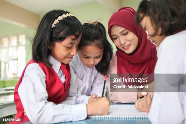 a female teacher teaching a group of students in a classroom - asian teacher stock pictures, royalty-free photos & images