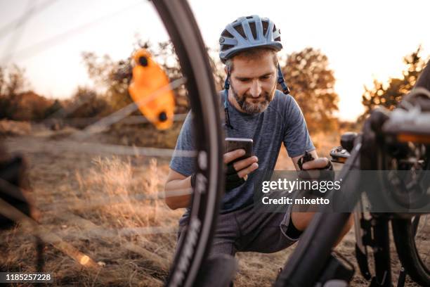biker mit telefon mit kaputtem fahrrad - fahrrad stock-fotos und bilder