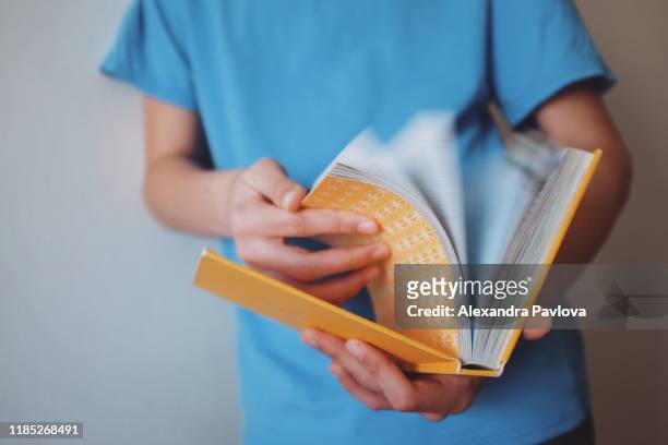 child flipping through pages of a yellow book, pages turning fast in motion blur - sfogliare libro foto e immagini stock