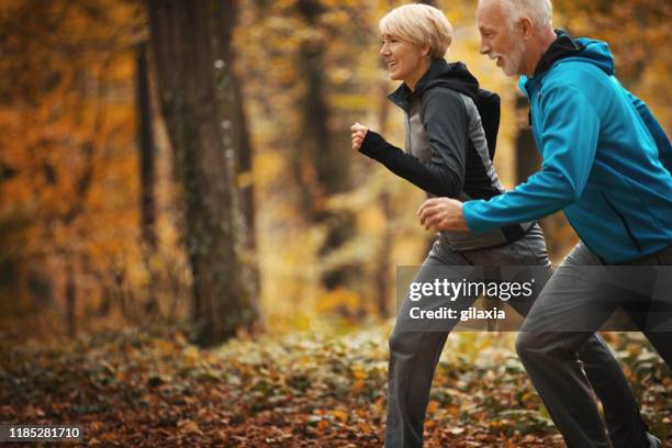 senior couple jogging in a forest. - november 2 2017 stock pictures, royalty-free photos & images