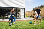 Parents playing soccer with kids in backyard.