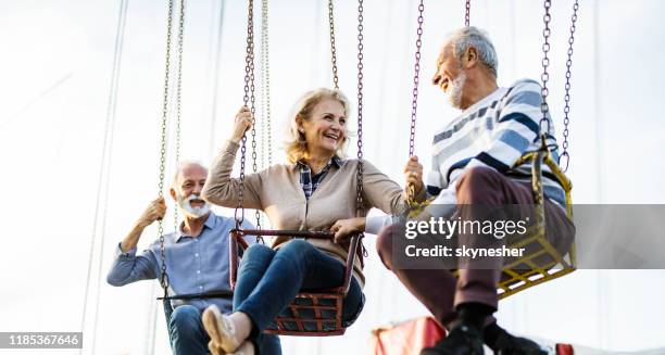 panoramic view of happy senior couple talking on chain swing ride. - carousel swings stock pictures, royalty-free photos & images