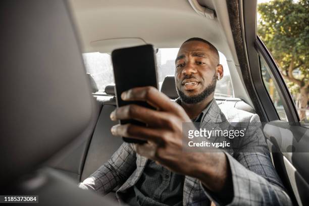 empresario africano montando en un coche en el asiento trasero y mensajes de texto - kunst, kultur und unterhaltung fotografías e imágenes de stock