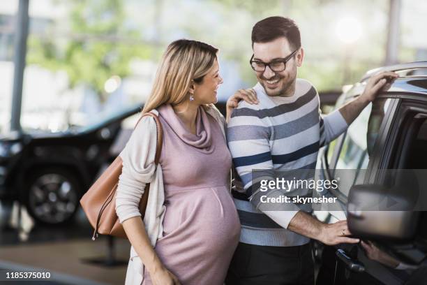 happy pregnant couple talking while buying a new car in a showroom. - pregnant woman car stock pictures, royalty-free photos & images
